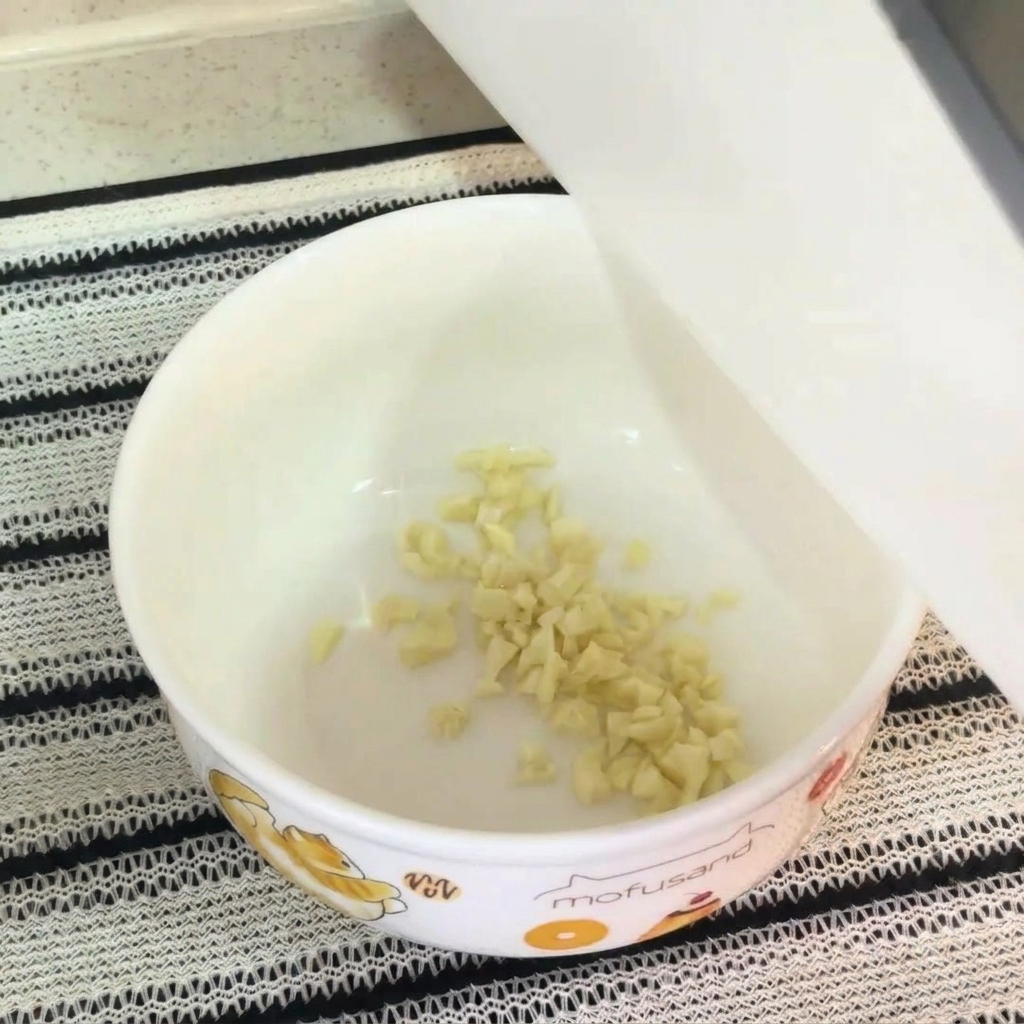 Primer plano de un bol blanco con ajo picado, yema de huevo cruda, condimento para fideos y mayonesa, listos para mezclarse.