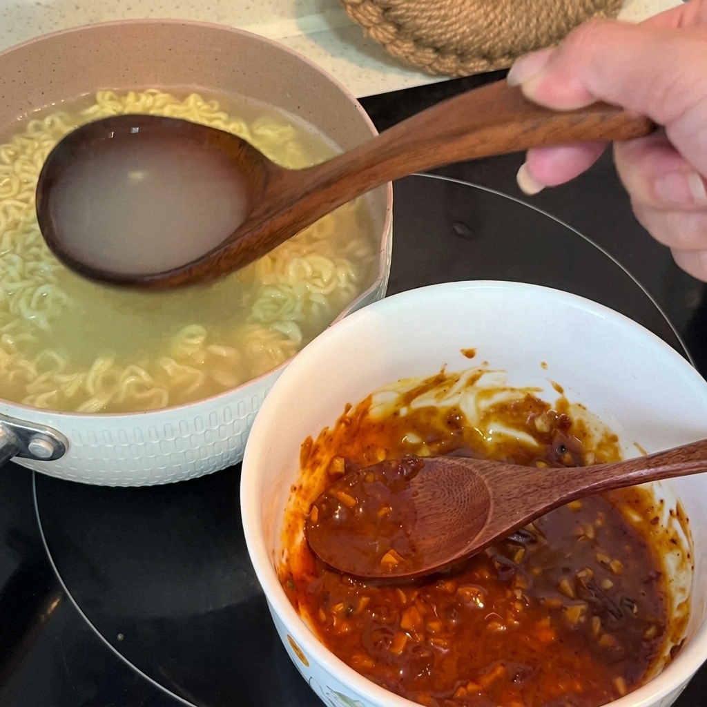 Agua caliente de los fideos vertiéndose desde un cazo de madera a un bol que contiene la pasta de condimentos.