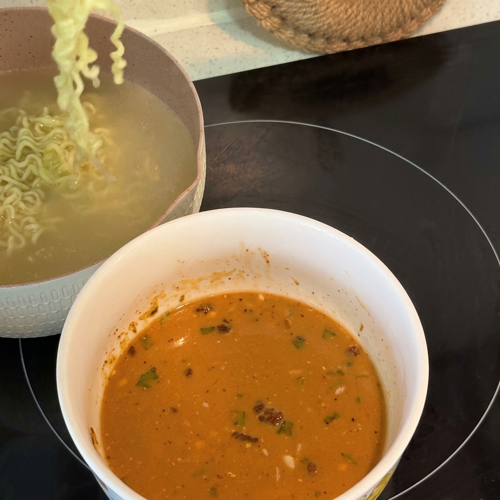 Fideos ramen rizados ya cocidos siendo levantados y transferidos a un bol lleno de una base de sopa cremosa y emulsionada.