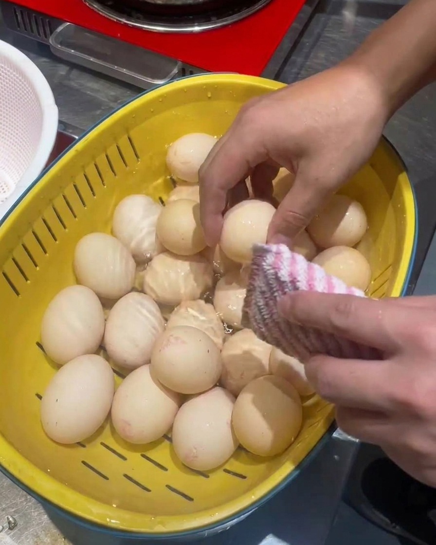 Huevos siendo limpiados en un colador amarillo con una esponja suave.