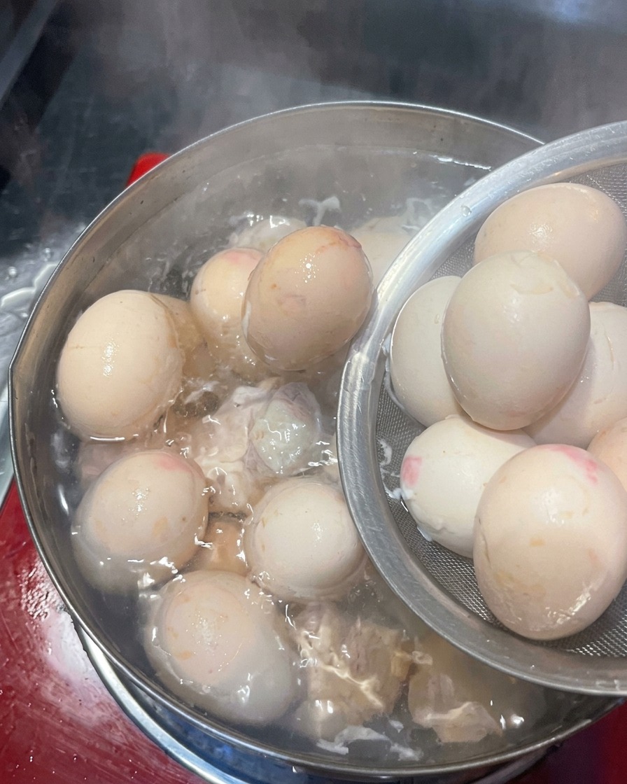 Huevos cocidos siendo trasladados de una olla a un recipiente con agua y hielo.