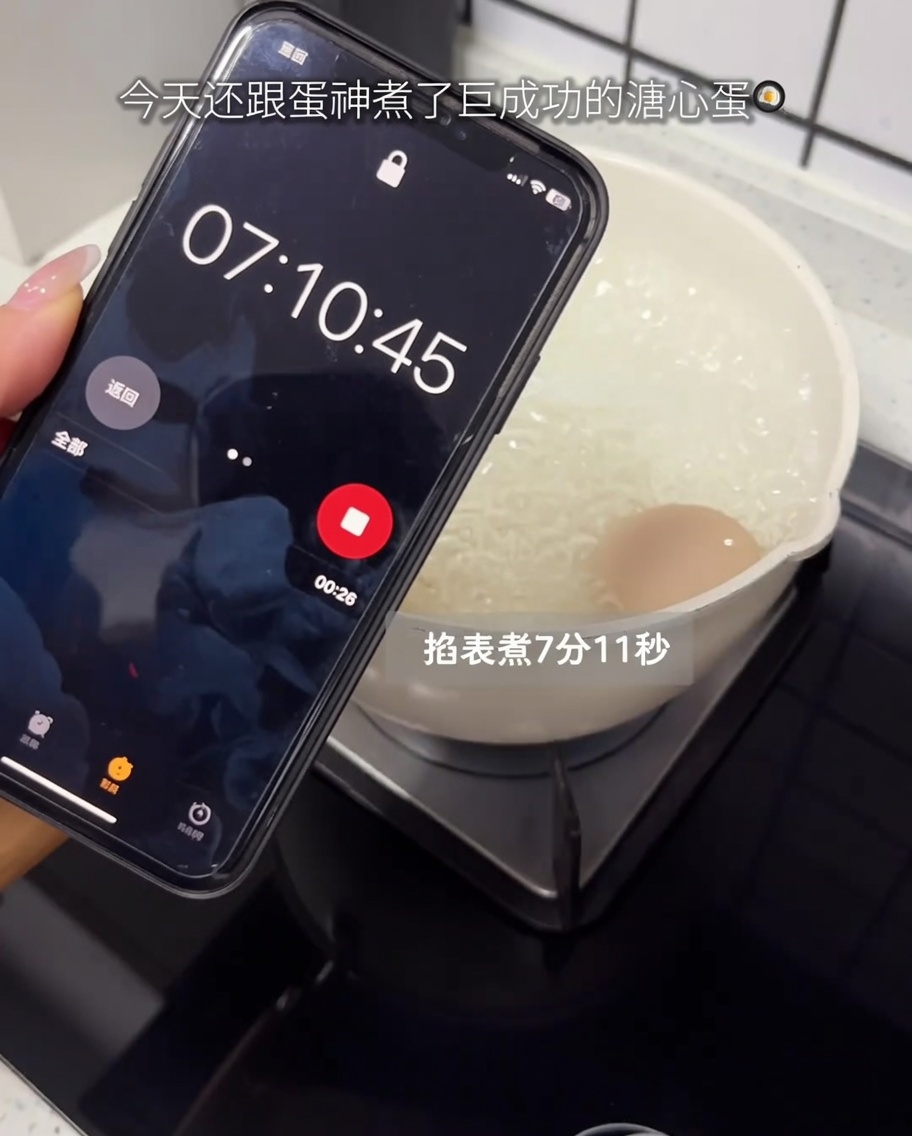 Un huevo crudo hirviendo en una olla sobre la estufa con un temporizador de smartphone en primer plano.