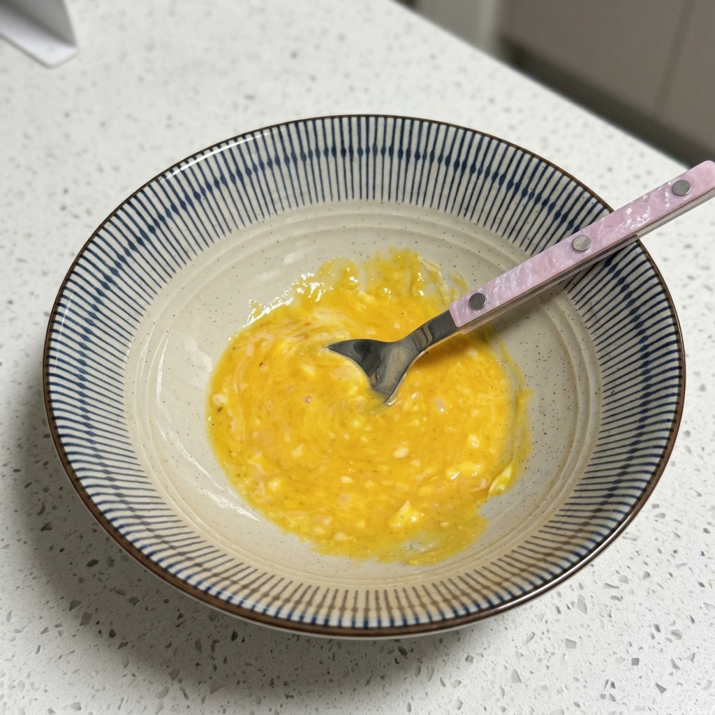 Un tazón con una base de caldo amarilla y cremosa siendo revuelta con una cuchara.