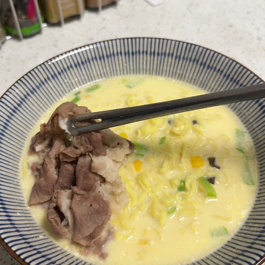 Una cucharada de granos de maíz dorados siendo espolvoreados sobre un tazón de ramen.