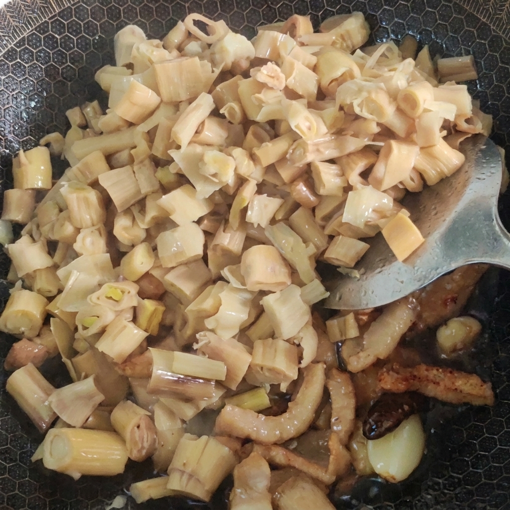 Agua y mostaza encurtida siendo añadidas al wok con cerdo y bambú salteados.