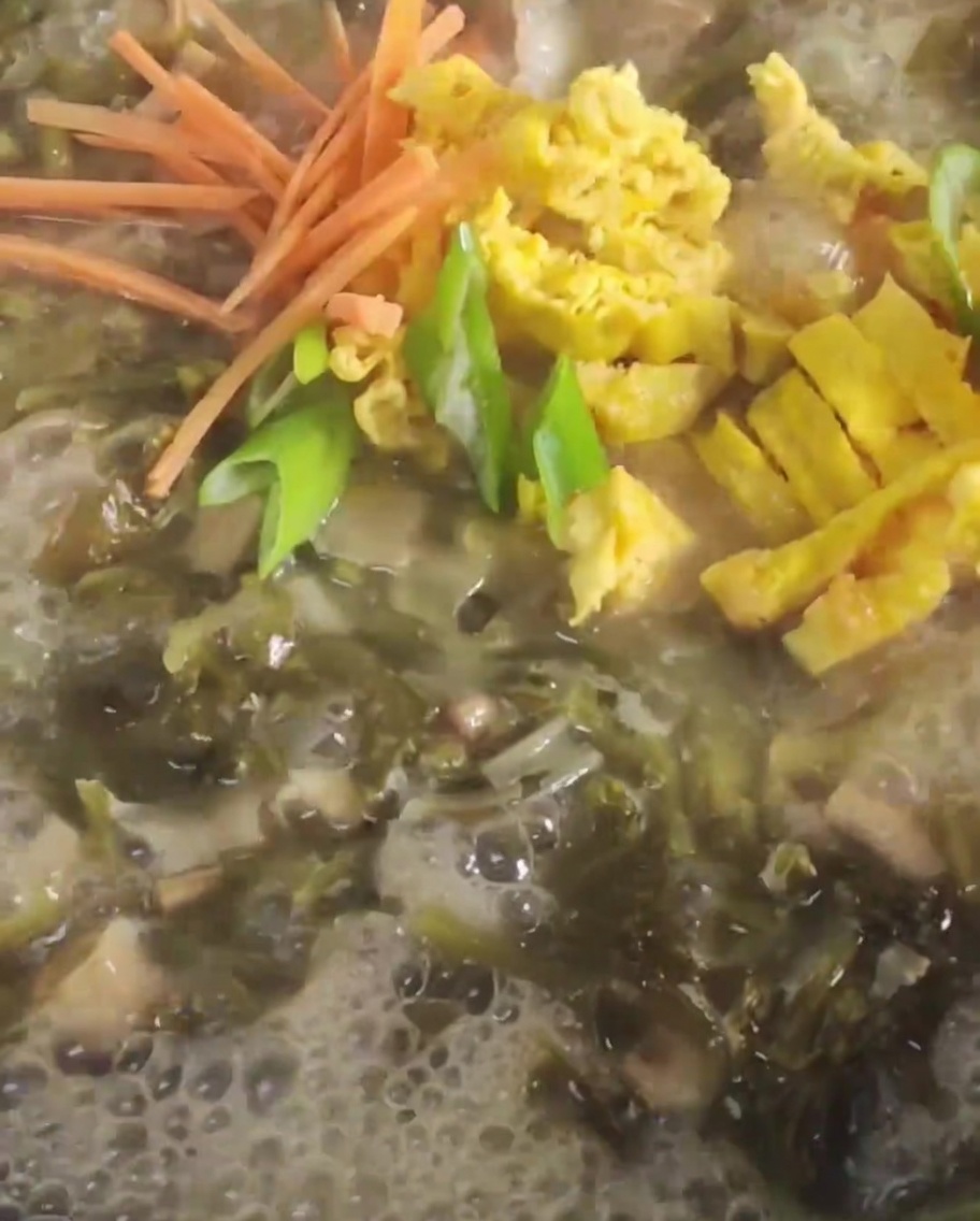 Zanahoria y huevo frito en tiras siendo añadidos a un caldo burbujeante con mostaza.