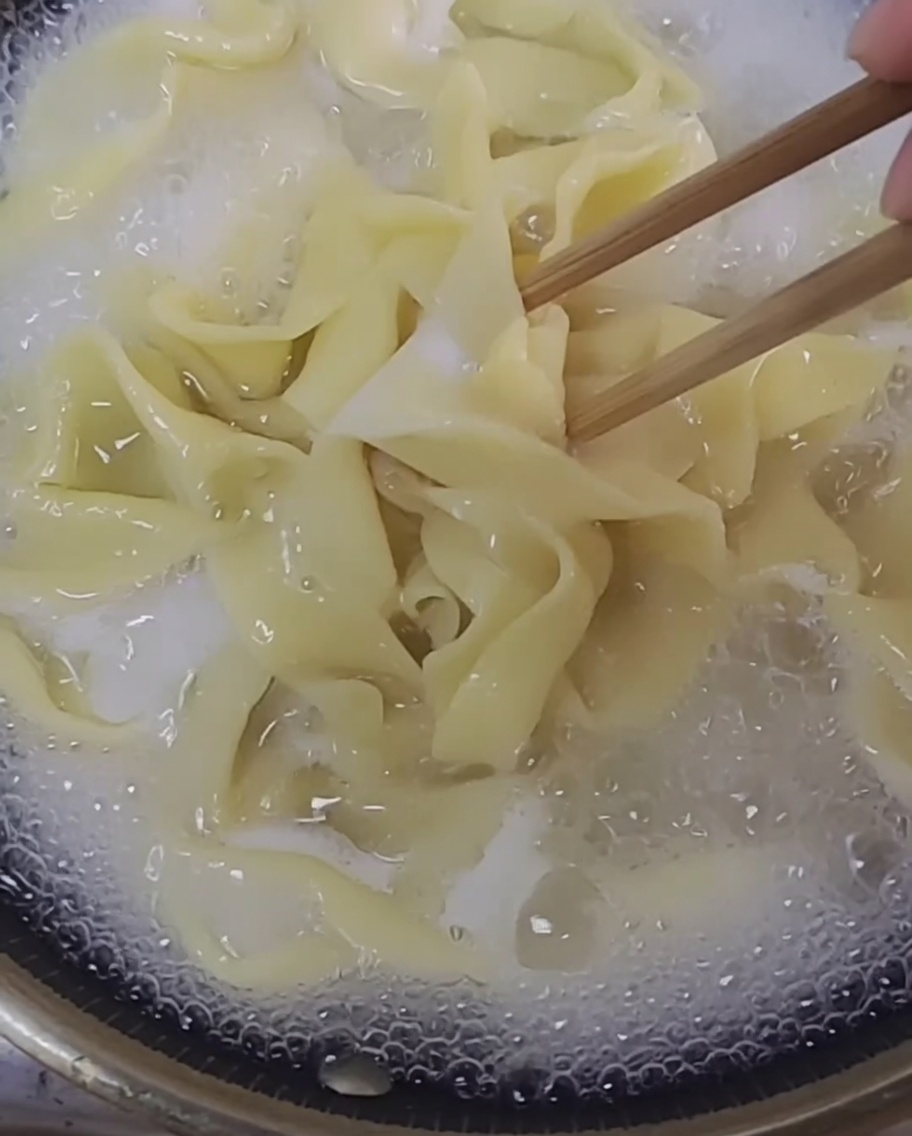 Hebras de fideos recién hechos hirviendo en una olla de agua clara.