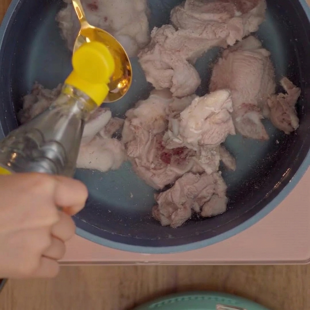 Una cucharada de vinagre blanco vertiéndose en una olla con huesos de cerdo.