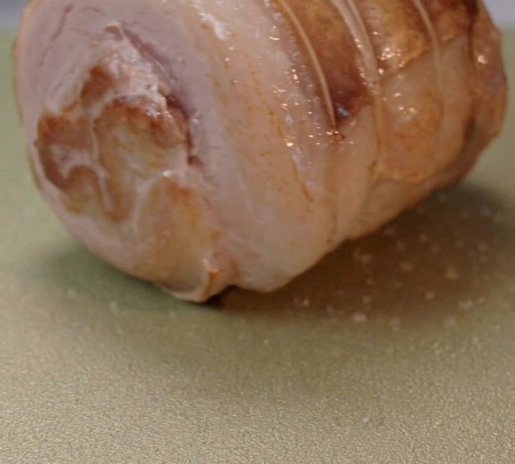Panceta de cerdo enrollada dorándose en una sartén con aceite caliente.