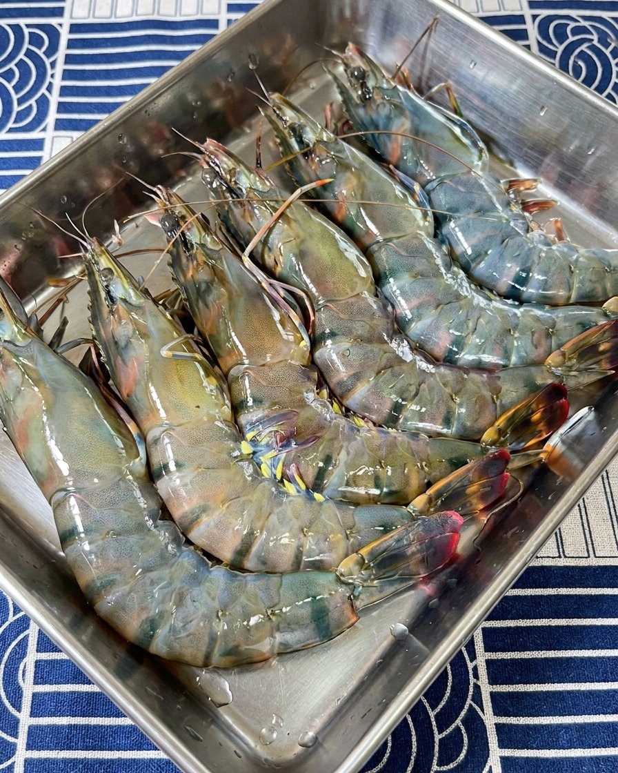 Una colección de cabezas y cáscaras de gamba tigre negra crudas en una bandeja de acero inoxidable.