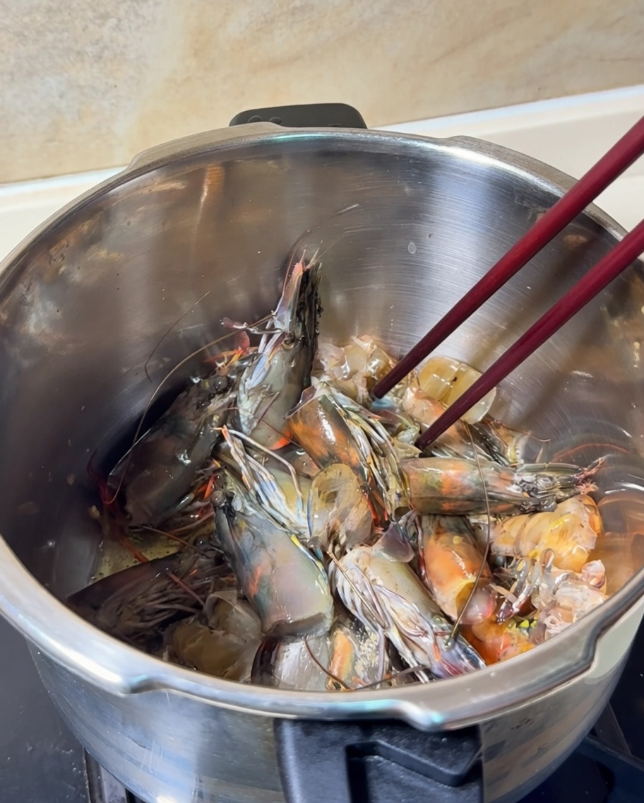 Cabezas y cáscaras de gamba sofriéndose en una olla, tornándose de un color naranja brillante.