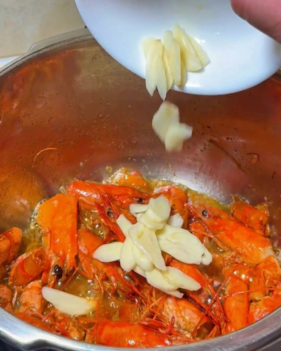 Ajo y cebolla cortados siendo añadidos a la olla con las cáscaras de gamba fritas.