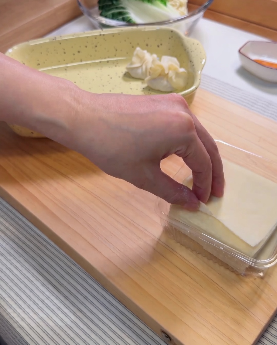 Una masa de wonton cruda en la palma de la mano con una porción de relleno de camarones lista para cerrar.