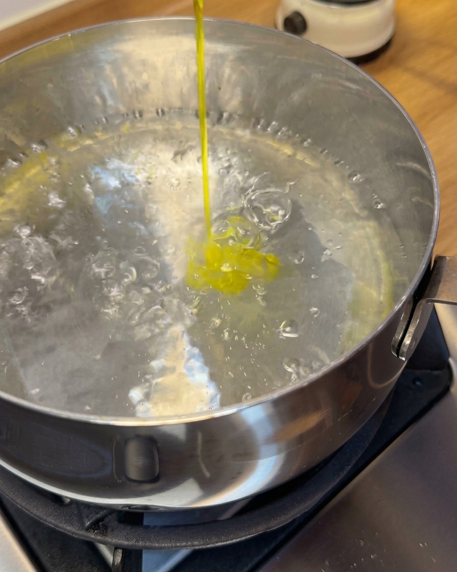 Wontons de camarones crudos siendo introducidos en una olla con agua hirviendo usando una espumadera.