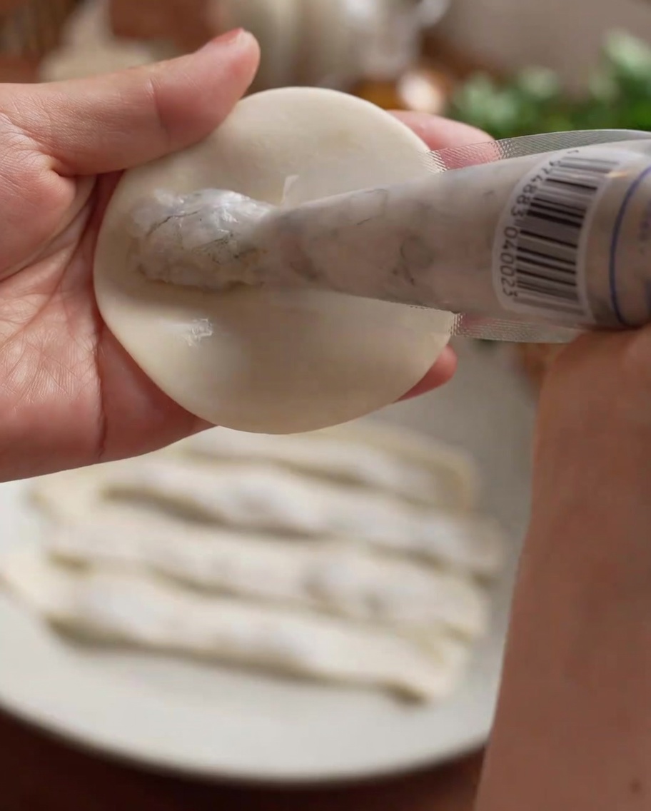 Pasta de camarones siendo aplicada con manga pastelera en línea recta sobre el centro de la masa.