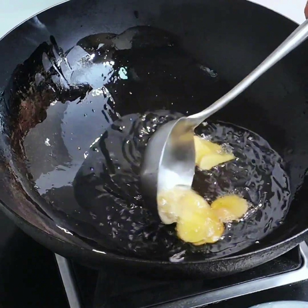Rodajas de jengibre y cabezas de camarón sofriéndose en un wok con aceite caliente.