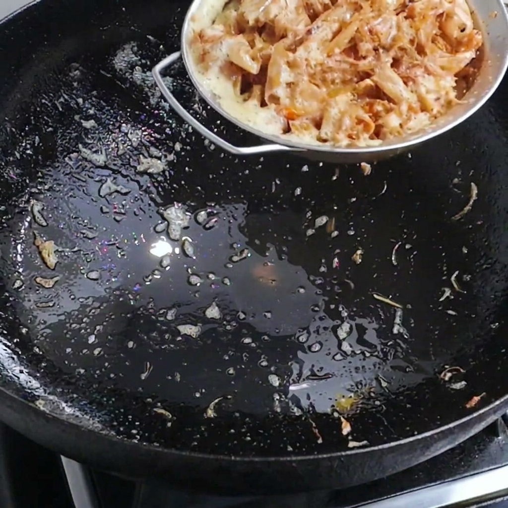 Agua caliente siendo vertida en un wok que contiene cáscaras de camarón para crear un caldo sabroso.