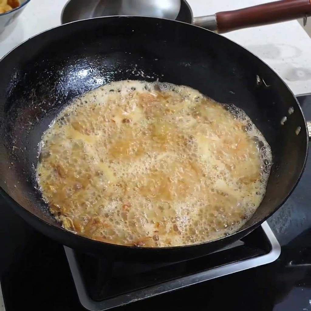 Sal siendo espolvoreada en un caldo de camarón dorado burbujeante.
