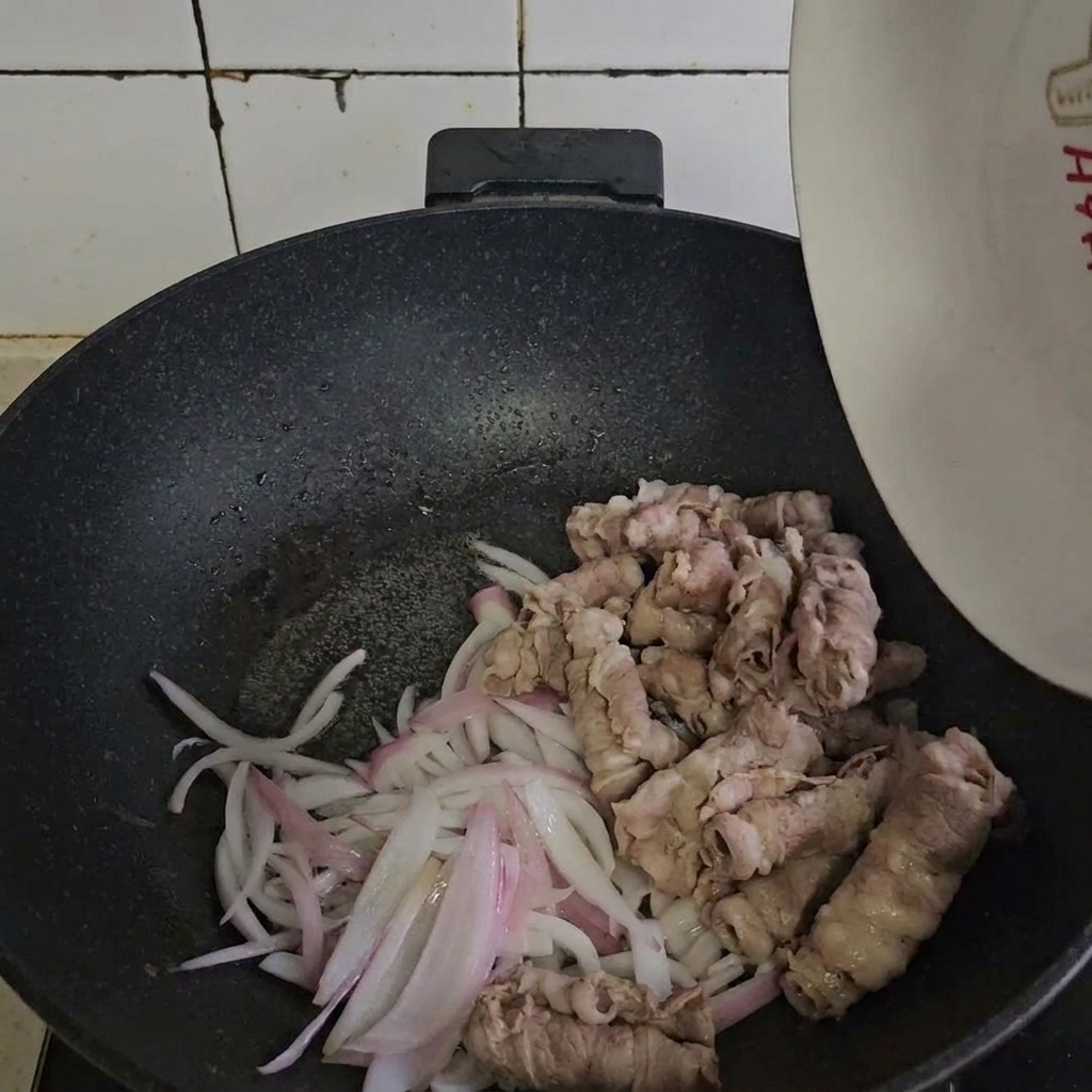 Rollos de carne blanqueados mezclándose con las cebollas salteadas en una sartén.