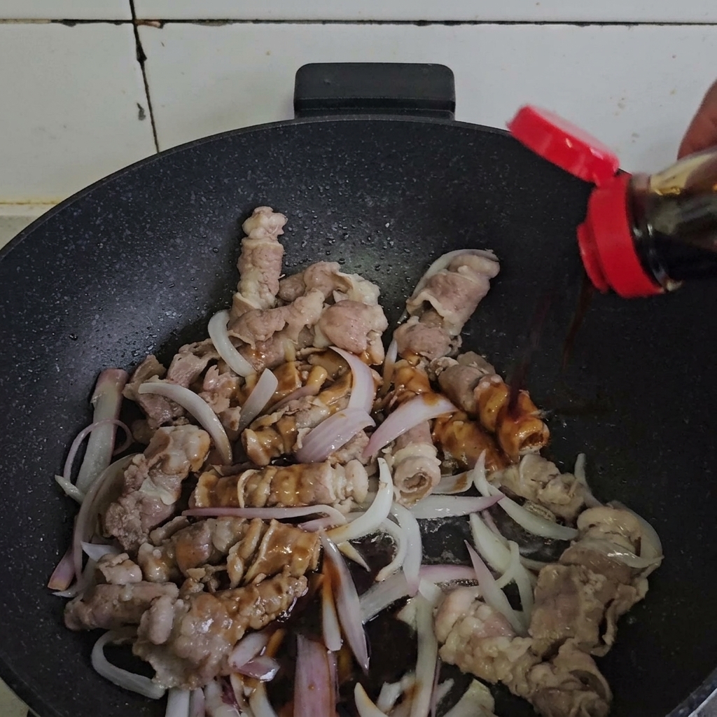 Carne y cebollas mezclándose con la salsa en una sartén caliente.