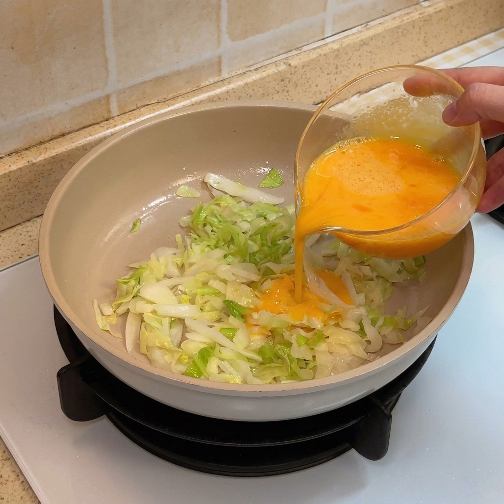 Huevos siendo vertidos sobre repollo salteado en una sartén antiadherente.