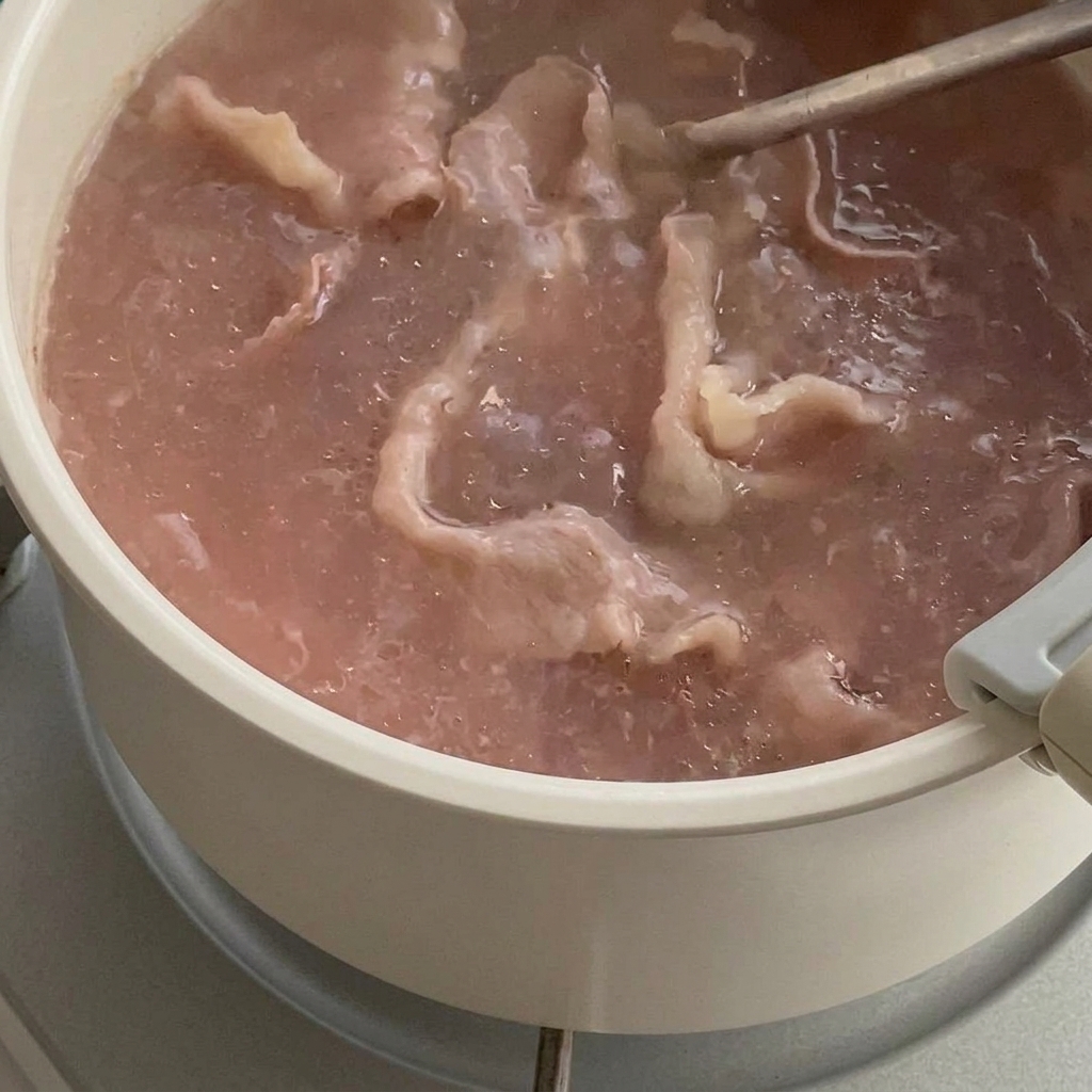 Lonchas de ternera parcialmente cocidas en agua hirviendo, siendo retiradas con un colador.