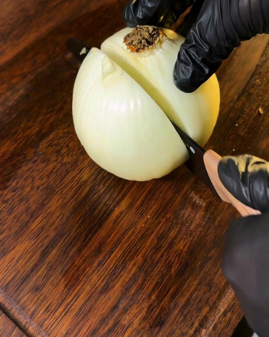 Una cebolla siendo cortada sobre una tabla de madera, lista para usar.