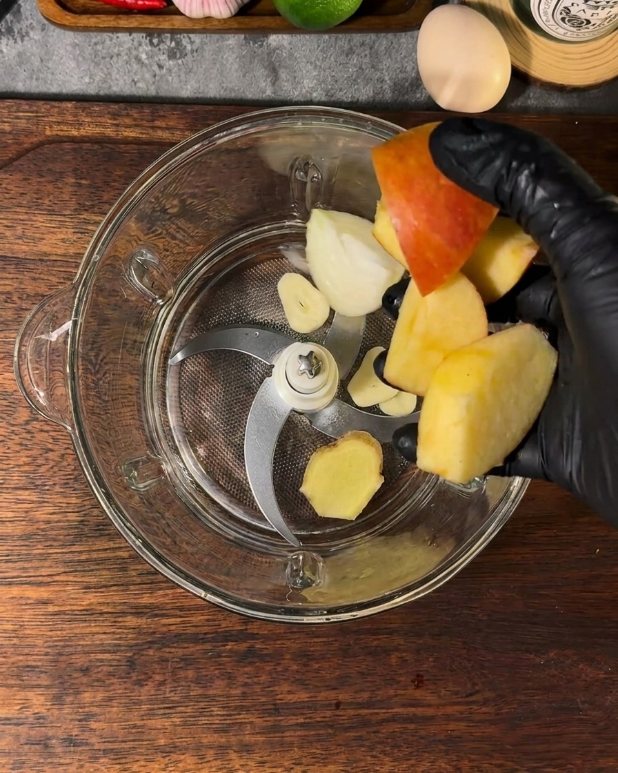 Un vaso de batidora con trozos de manzana, cebolla, ajo, jengibre y agua.