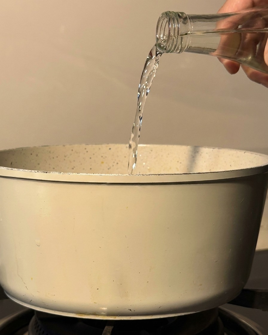 Sake y mirin siendo vertidos desde una botella de cristal en una olla sobre la estufa.