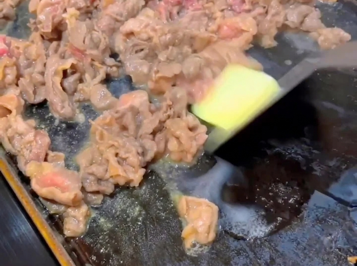 Un pequeño cuadrado de mantequilla derritiéndose sobre rebanadas de carne parcialmente cocidas en una sartén plana caliente.