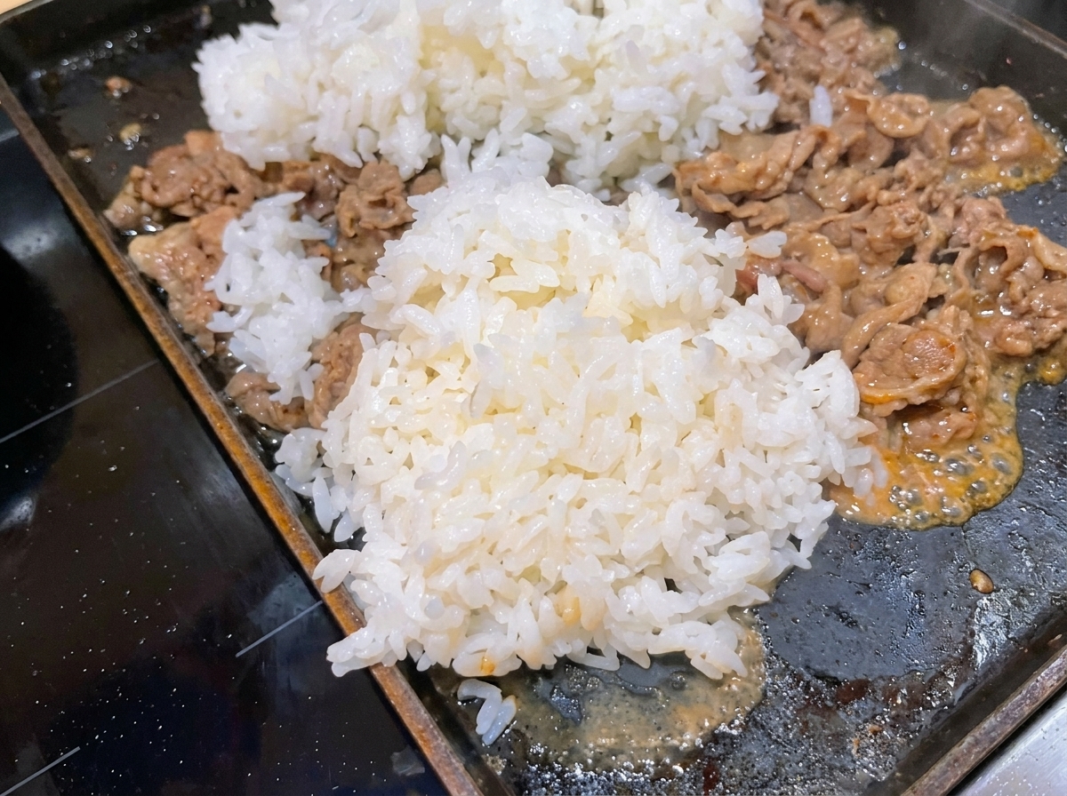 Un montículo generoso de arroz blanco cocido añadido a una sartén caliente donde se está cocinando la carne.
