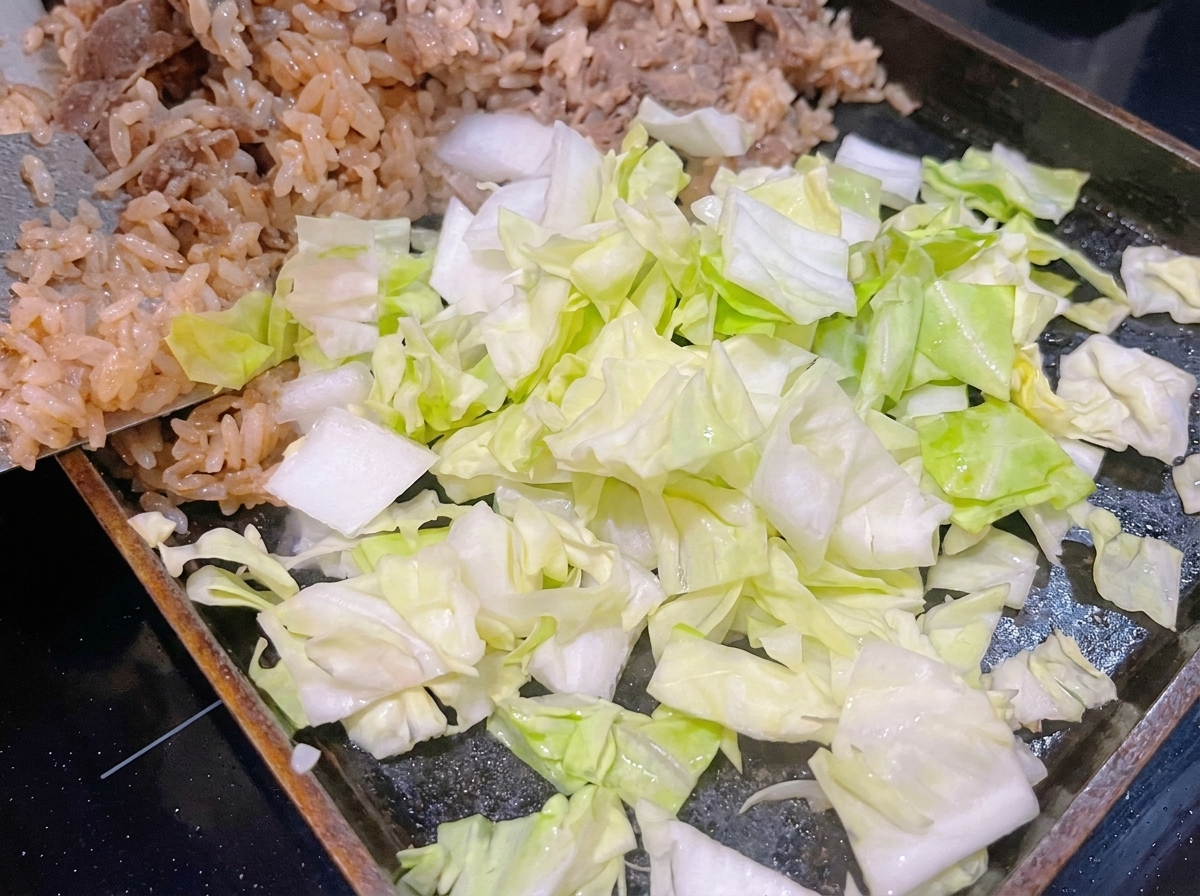 Repollo verde recién picado colocado sobre el arroz blanco y la carne en una sartén caliente.