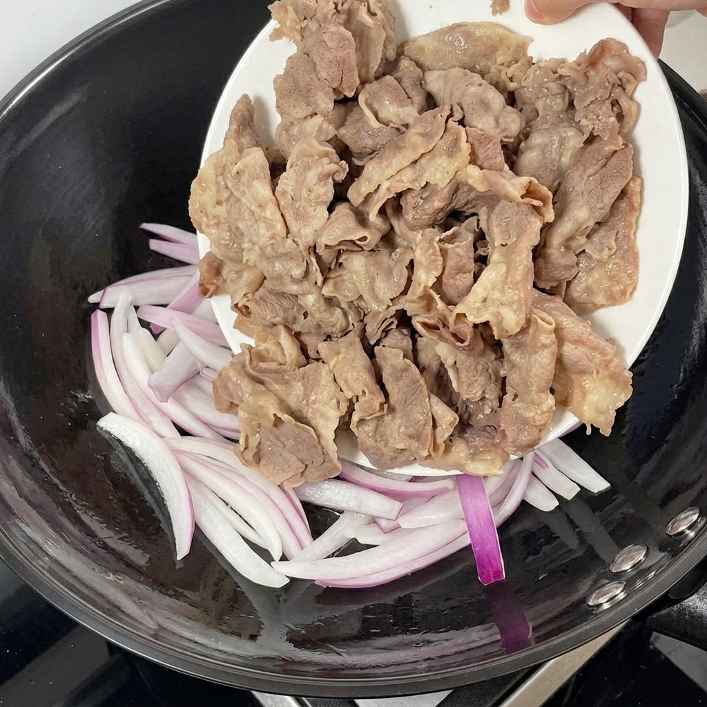Carne escaldada añadiéndose a una sartén con cebolla morada salteada.