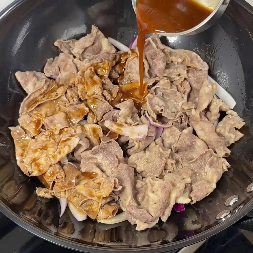 Salsa teriyaki oscura vertiéndose sobre la carne y cebolla en un wok.