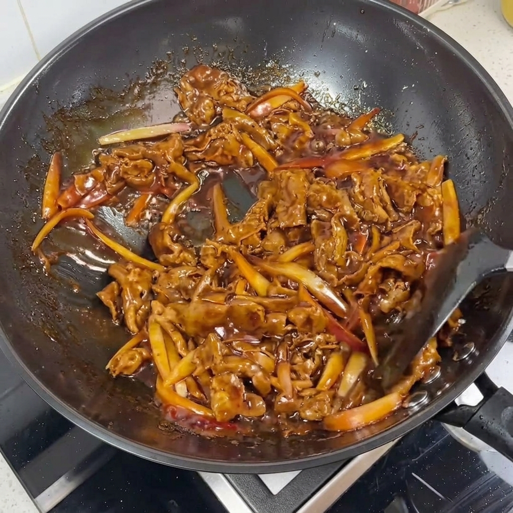 Primer plano de carne y tiras de cebolla glaseándose en una salsa teriyaki brillante en un wok.