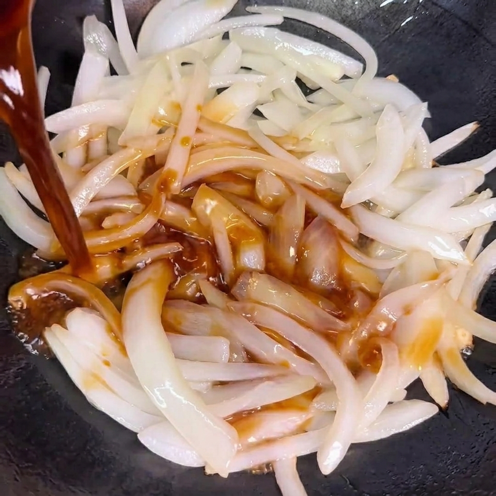 Salsa siendo vertida sobre las cebollas salteadas en un wok.
