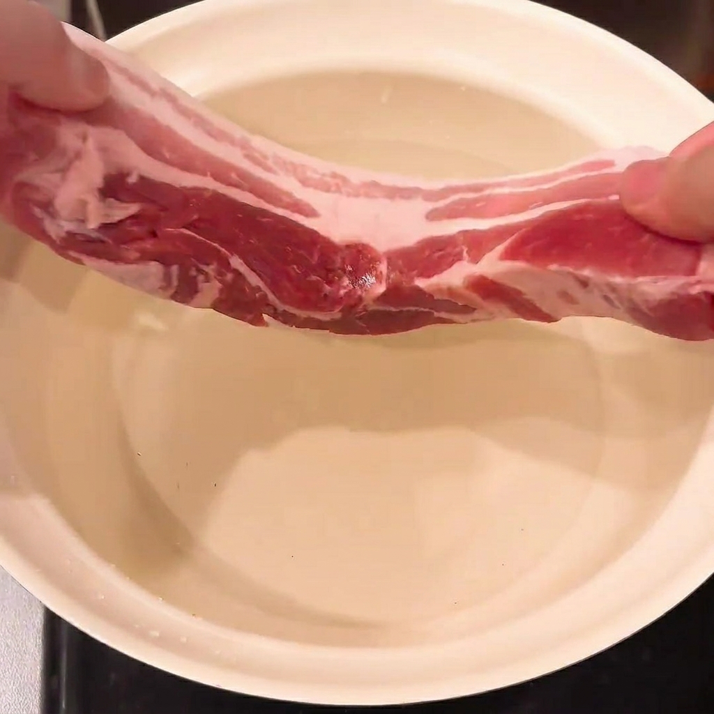 Panceta de cerdo, cebolla verde y jengibre sumergidos en una olla con agua, listos para escaldar.