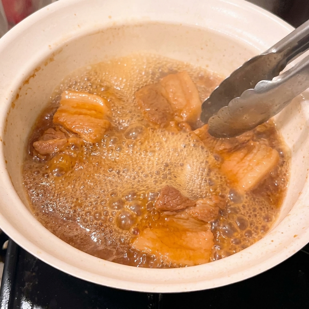 Primer plano de trozos de cerdo tiernos cocinándose en un glaseado de miso espeso y burbujeante.