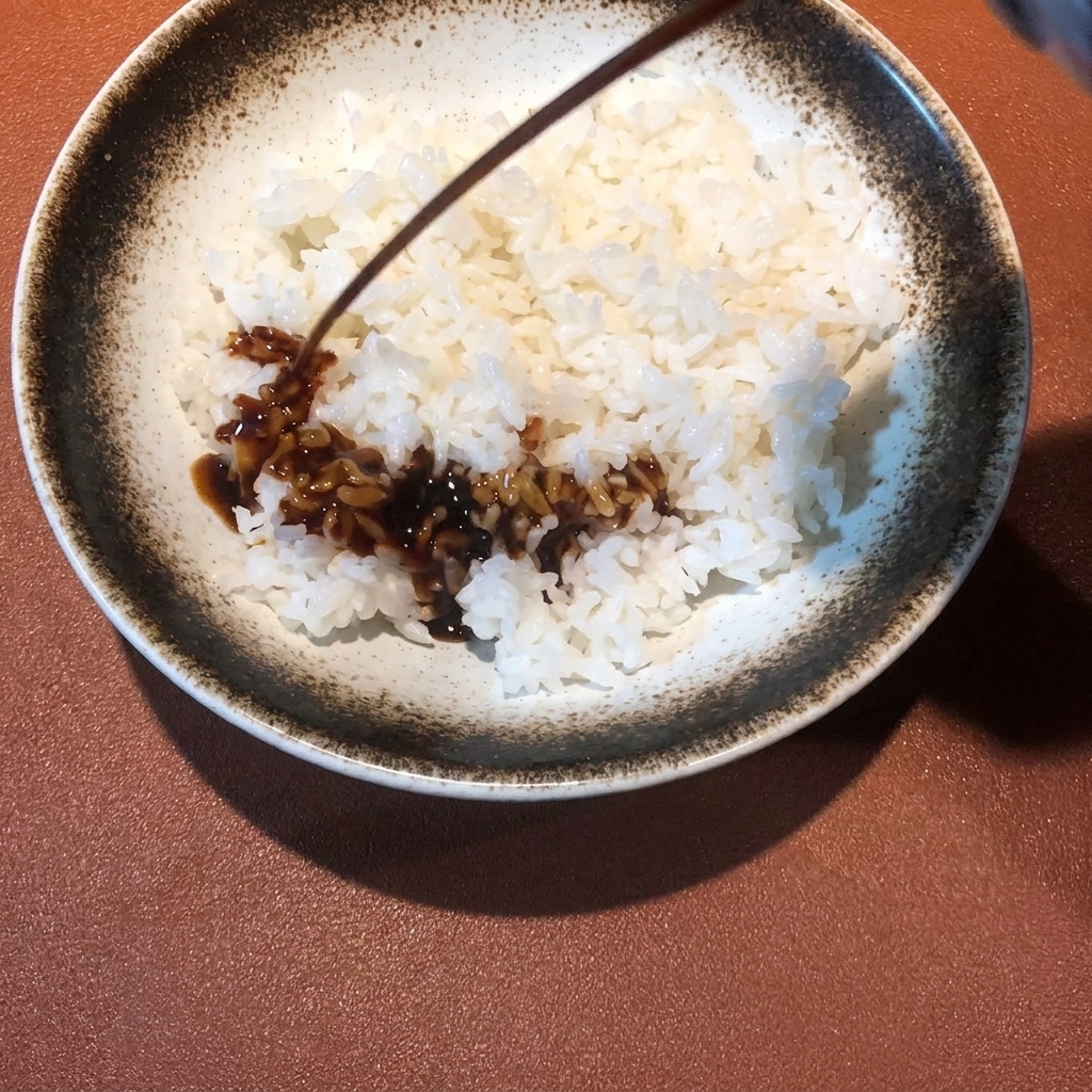 Salsa oscura siendo rociada sobre un tazón de arroz blanco al vapor.