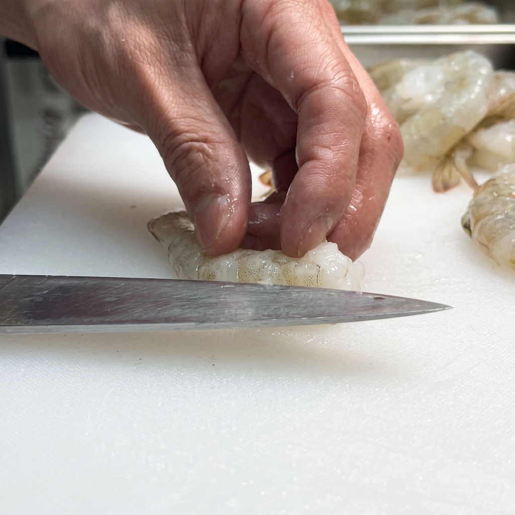 Primer plano de un cuchillo haciendo un corte a lo largo de la espalda de un camarón crudo.