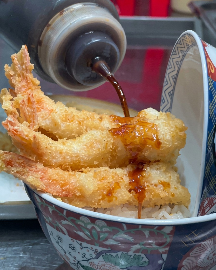 Salsa oscura siendo rociada desde una botella sobre los camarones fritos.