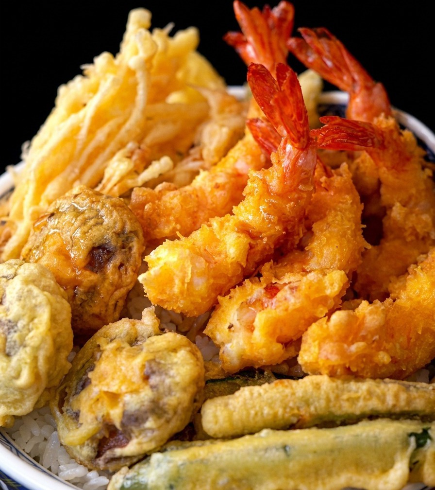 Un tazón de arroz con tempura terminado, coronado con camarones fritos crujientes y verduras.