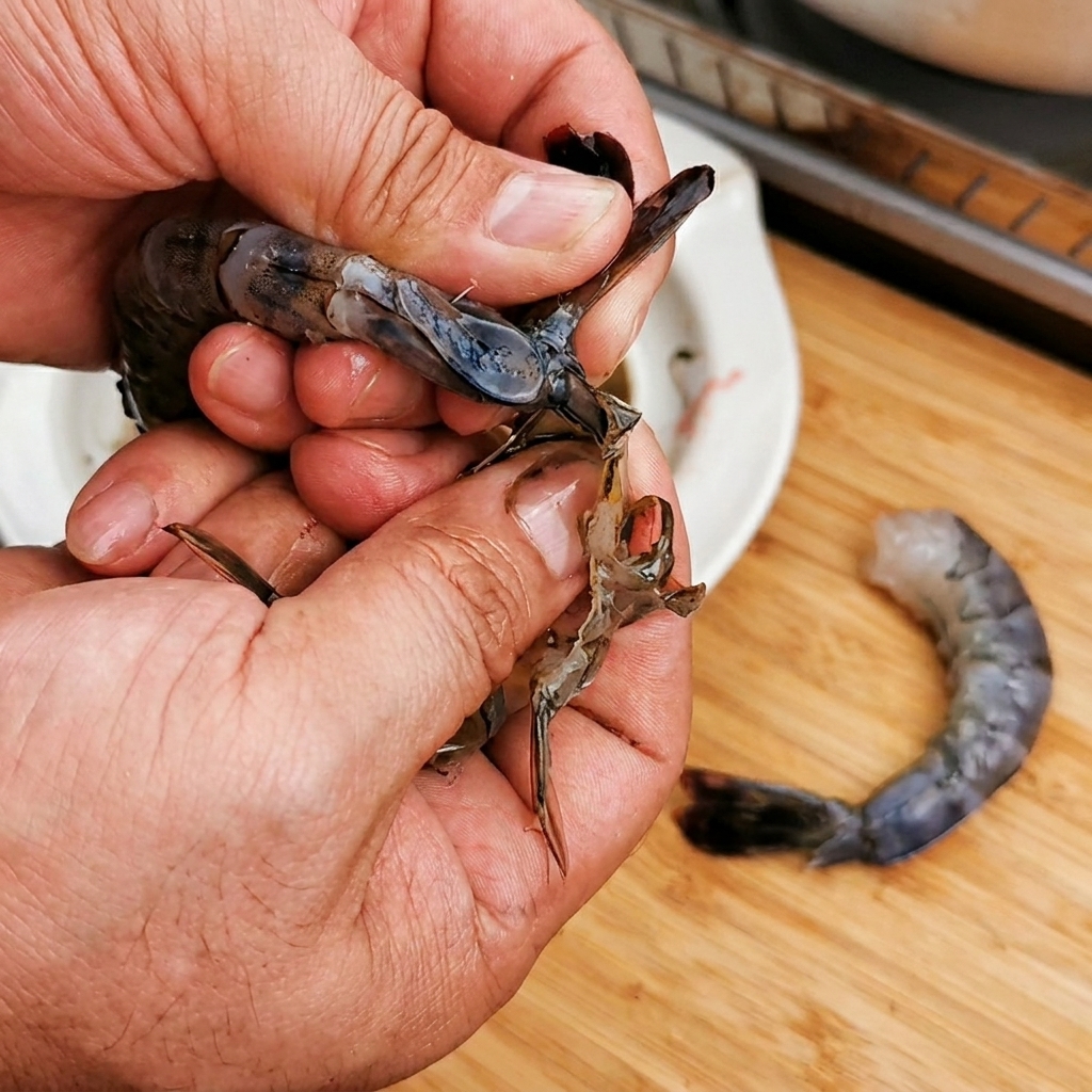 Primer plano de manos pelando un camarón crudo manteniendo la cola intacta.