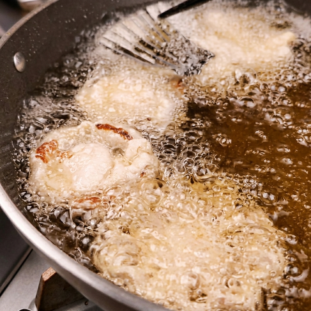 Verduras rebozadas friéndose en una sartén con aceite caliente.