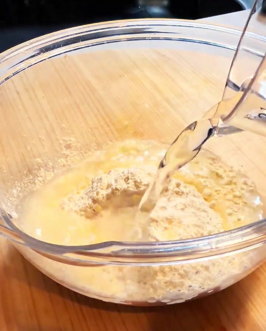 Un tazón de vidrio que contiene harina para tempura y agua, siendo batido para formar una masa suave y ligera.