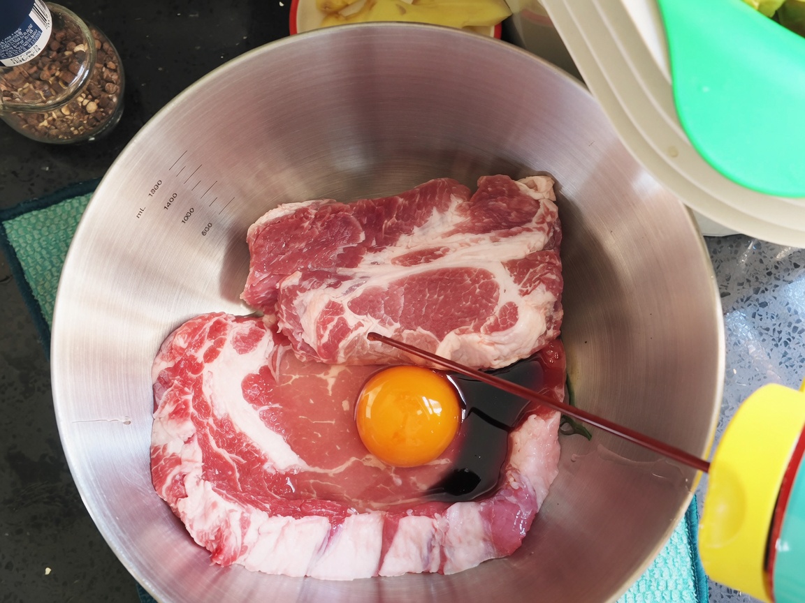 Salsa de soja oscura y condimentos siendo vertidos sobre las chuletas de cerdo y el huevo en un tazón.