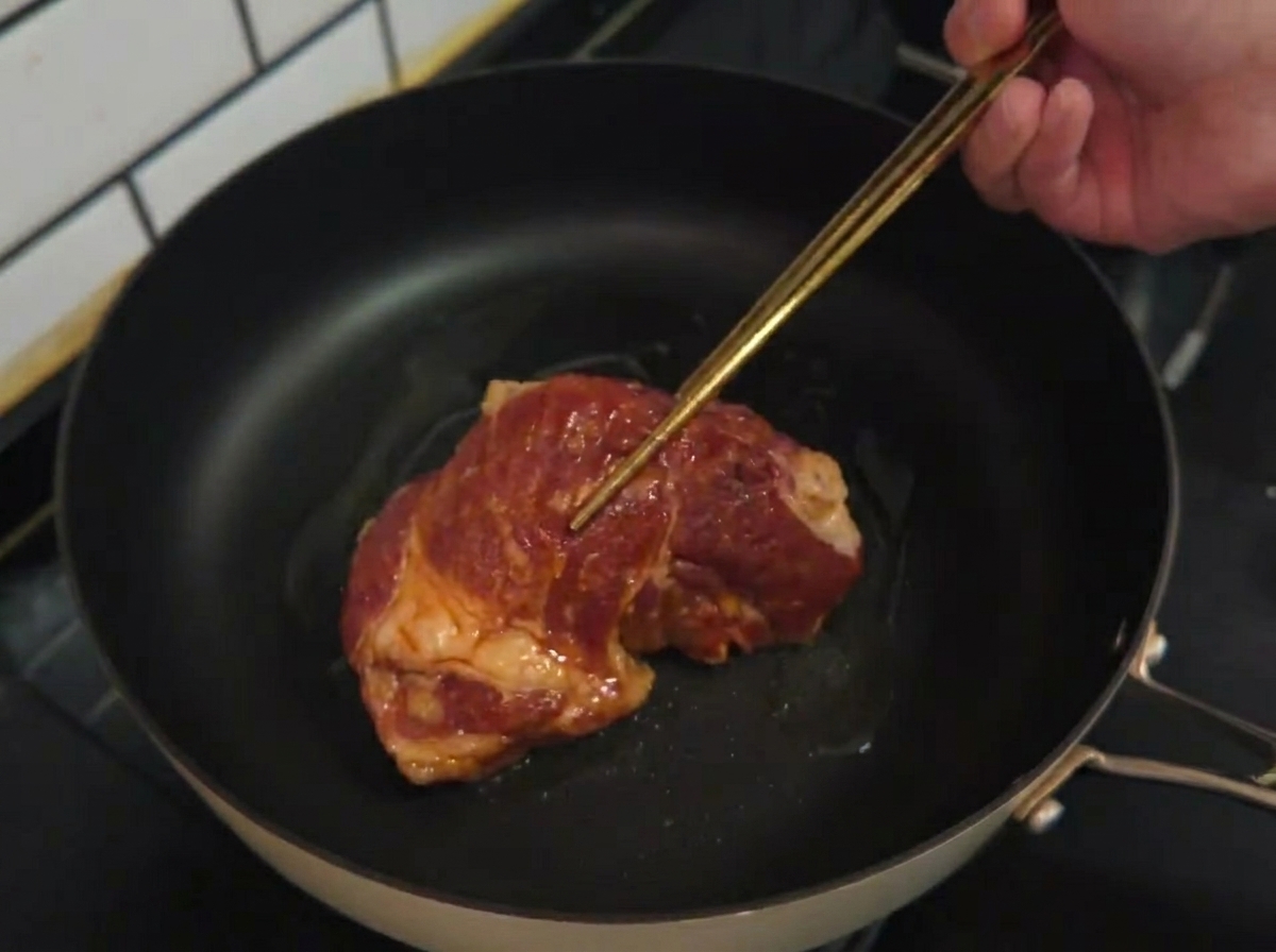 Chuleta de cerdo marinada colocada en una sartén caliente con aceite de cocina.
