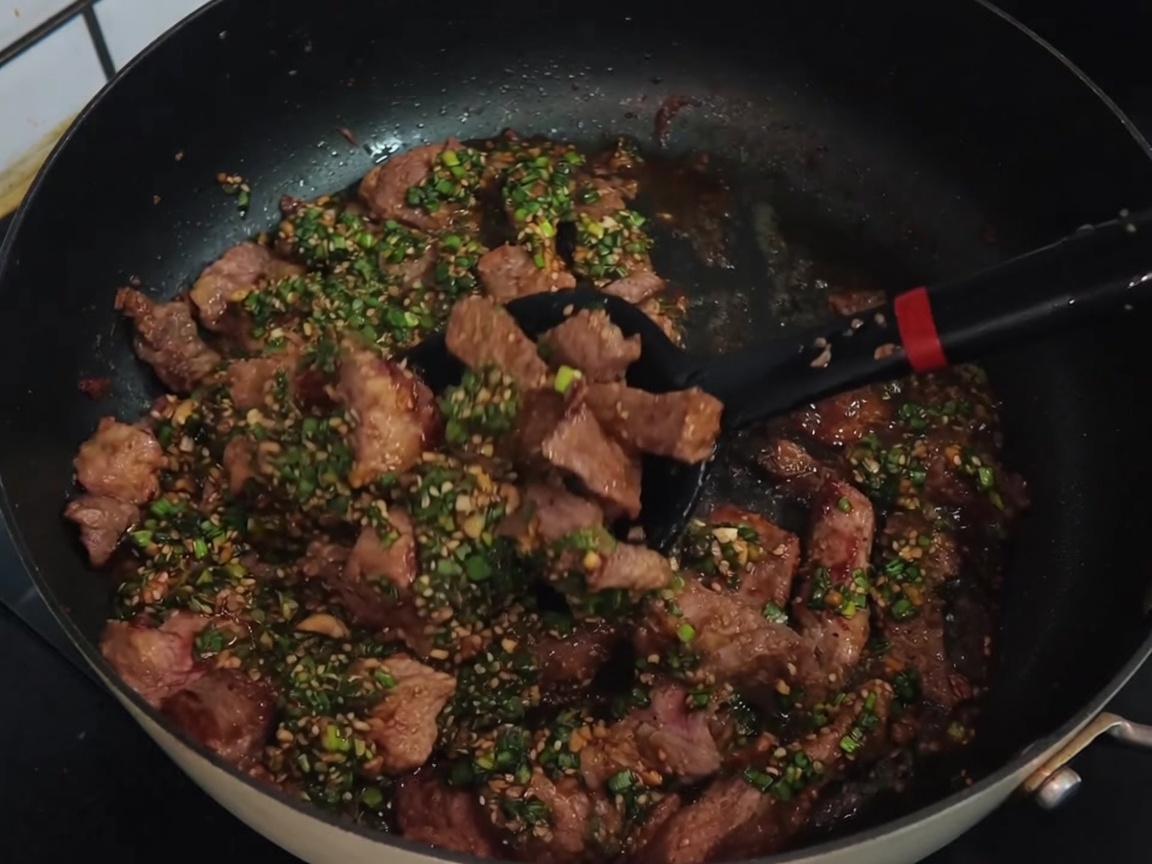 Una espátula negra mezclando tiras de cerdo con la salsa de cebollino en una sartén antiadherente.
