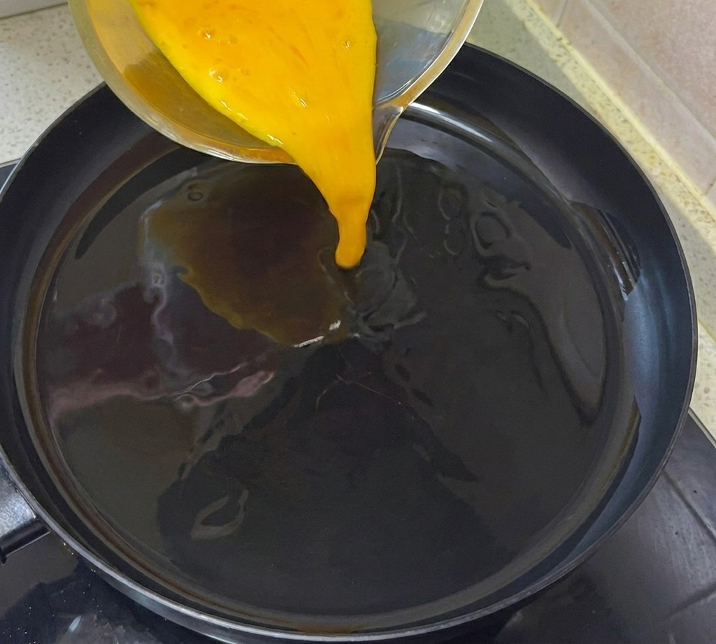 Mezcla de huevo siendo vertida en una sartén precalentada con aceite.