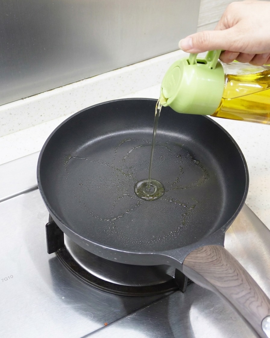 Primer plano de aceite siendo vertido en una sartén antiadherente precalentada, lista para la anguila.